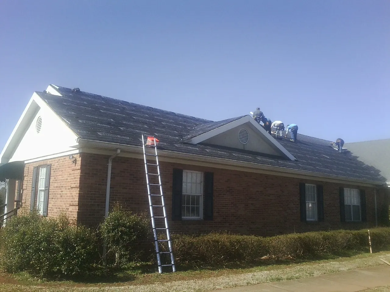 Crew tearing shingles off a brick ranch roof with a ladder set — Metal Roof Repair work by our crew in Beech Grove