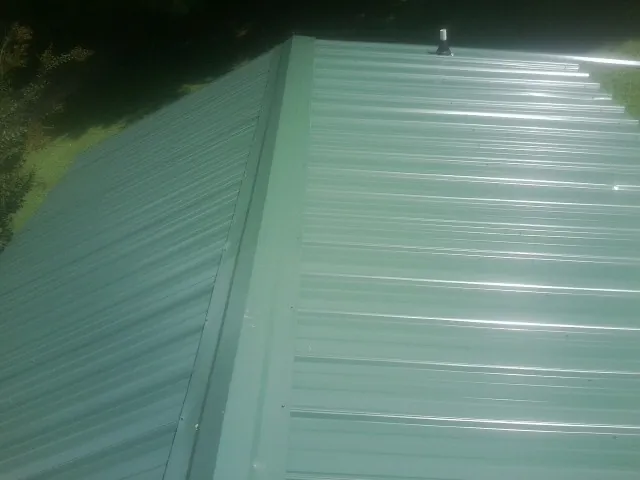 New green metal panels meeting at the ridge of a roof — Flat Roof Repair work by our crew in Beech Grove