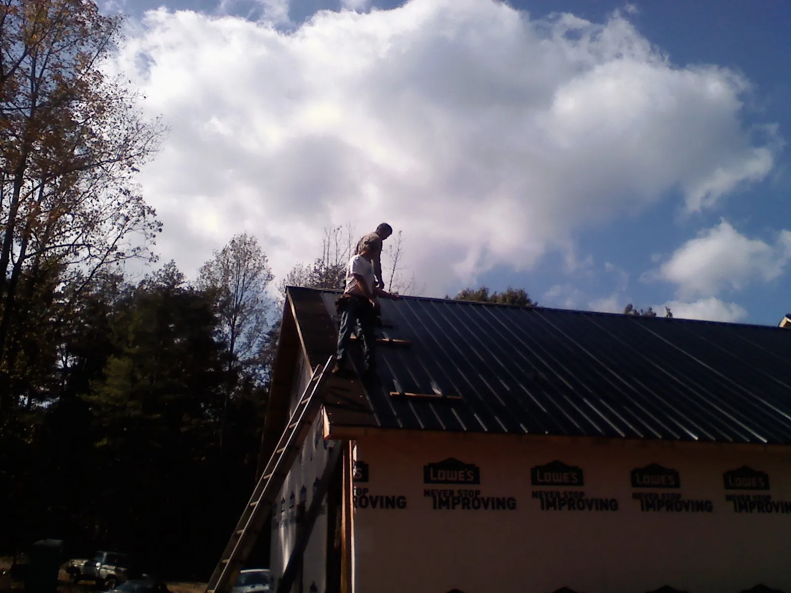 Roofer fastening dark metal panels high against a cloudy sky, from a Roof Inspection job in Beech Grove