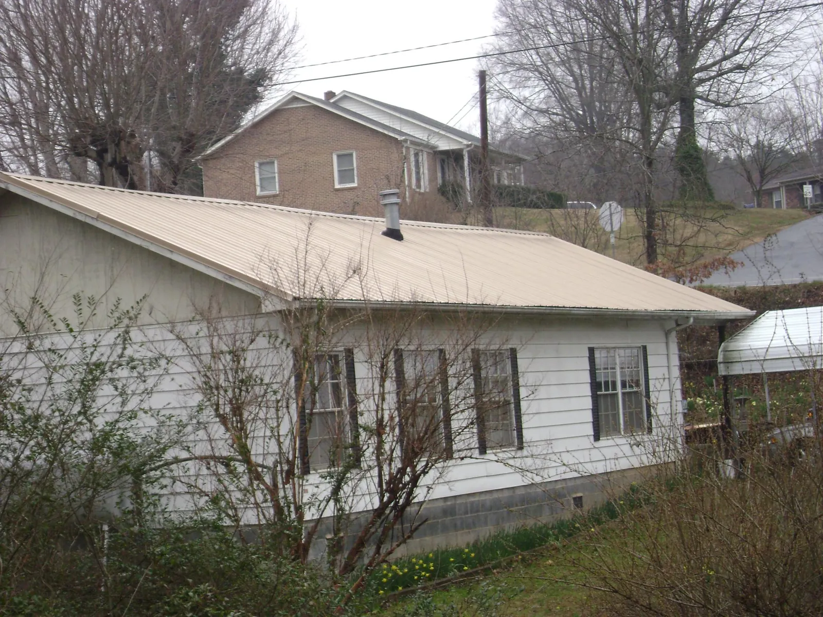 Tan metal roof on a white sided house set into a hillside — Commercial Roofing by Roofing Brothers in Beech Grove