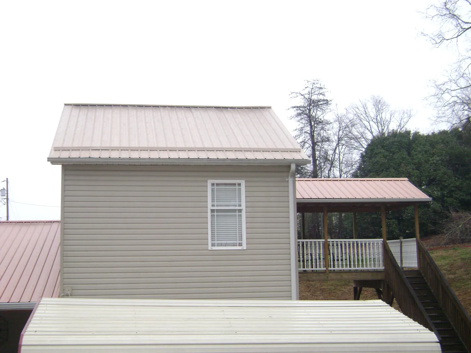 Tan metal roofs on a two story addition and attached porch, from a Roof Replacement job in Beech Grove